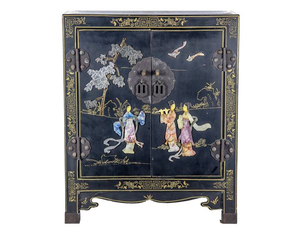 Japanese casket in black lacquered wood with oriental scroll inlays and life scenes in relief with applications of semi-precious stones and jade, two doors and a central shelf inside