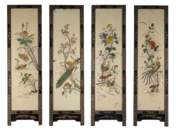 Lotto di quattro pannelli giapponesi in legno ebanizzato decorati a rilievo con giade e pietre dure a motivi di fiori e volatili orientali