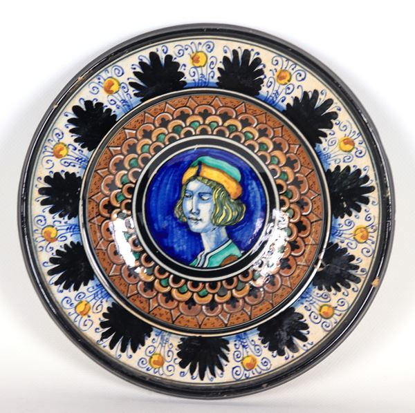 Wall plate in Pesaro majolica marked M.A.P. (Maiolica Artistica Pesarese 1930 - 1940), entirely decorated in blue, brown and green, in the center "Nobleman with hat". Glued breakage on the edge