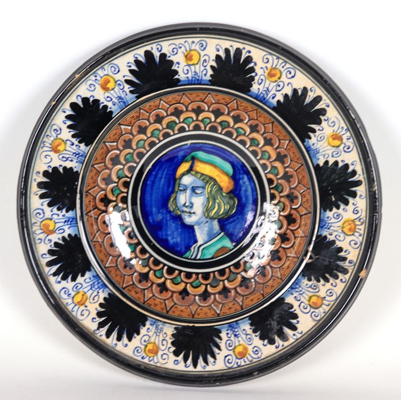 Piatto da muro in maiolica di Pesaro interamente decorato in blu, marrone e verde, al centro ritr...
