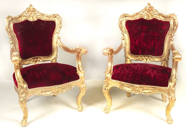 Pair of antique Neapolitan Louis Philippe armchairs in gilded and richly carved wood, with curved armrests and legs ending in lion's paws, covering in defective purple-red velvet. Defect in one armrest