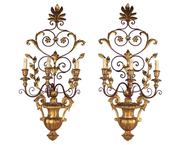 Coppia di appliques in legno dorato e ferro battuto a forma di anfore con rami e fiori, 3 luci ciascuna
