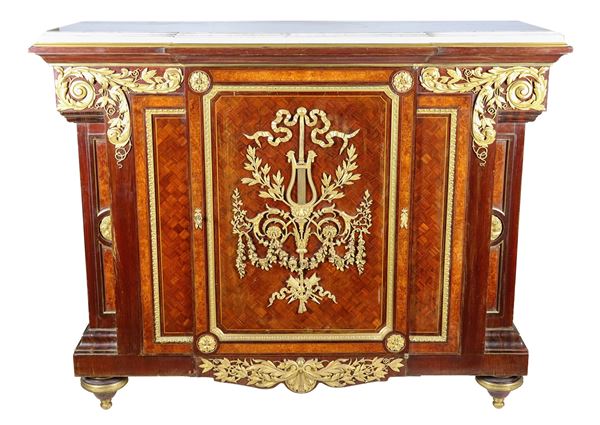 Antica servante francese Napoleone III (1852-1870) in bois de rose, mogano, ebano viola e tuja, con intarsi a marqueterie e fregi e guarnizioni in bronzo dorato e cesellato a motivi Luigi XVI di intrecci floreali, foglie d'acanto, fiocco con lira e rosoni. Uno sportello centrale e piano in marmo bianco statuario