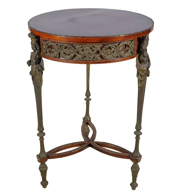 Round-shaped French gueridon in mahogany, bois de rose and purple ebony, with top inlaid with marqueterie and trimmings and friezes in embossed and chiseled bronze with Louis XVI motifs, three faceted legs joined by a shaped cross