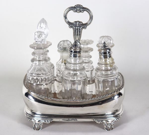 Ancient cruet from the Queen Victoria era in chiselled and embossed silver, supported by four curved feet, seven bottles in worked crystal with some slight defects and wooden base. London stamps 1839