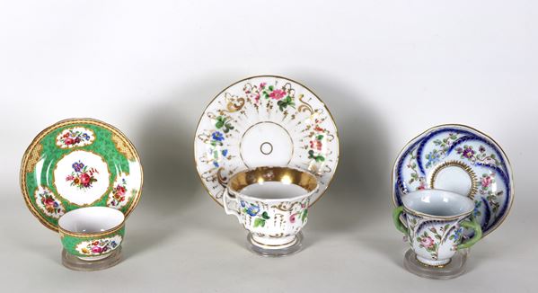 Lotto di tre antiche tazze con piattini in porcellana variopinta a motivi floreali, manifatture inglese e francese, forme, decori e misure differenti. La tazza più grande presenta sbeccatura al bordo
