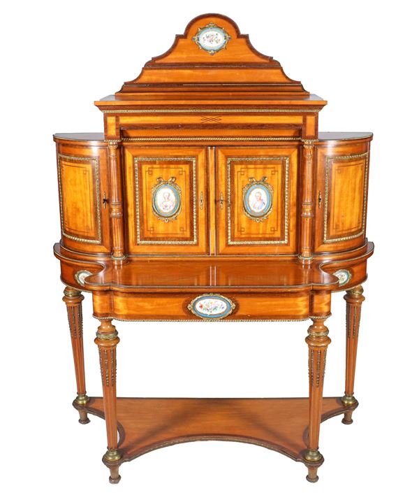 Antico bonheur du Jour francese Napoleone III (1852-1870) in legno satinato, con guarnizioni in metallo dorato e cesellato e applicazioni di placche ovali in porcellana di Sevres. La parte superiore a due sportelli centrali con montanti a colonnine e due sportelli semitondi ai lati, la parte inferiore a forma sagomata centinata con tiretto centrale e quattro gambe a cono riunite da piano sagomato