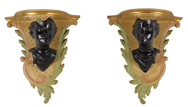 Coppia di piccole mensole da muro in legno decorato e laccato, con sculture ebanizzate di volti di bambini. Alcune scrostature sui piani