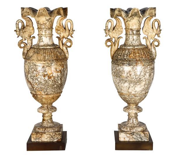 Coppia di vasi ad anfora in marmo di alabastro fiorito, con bordi frastagliati e manici con sculture di cigni, basi quadrangolari in metallo