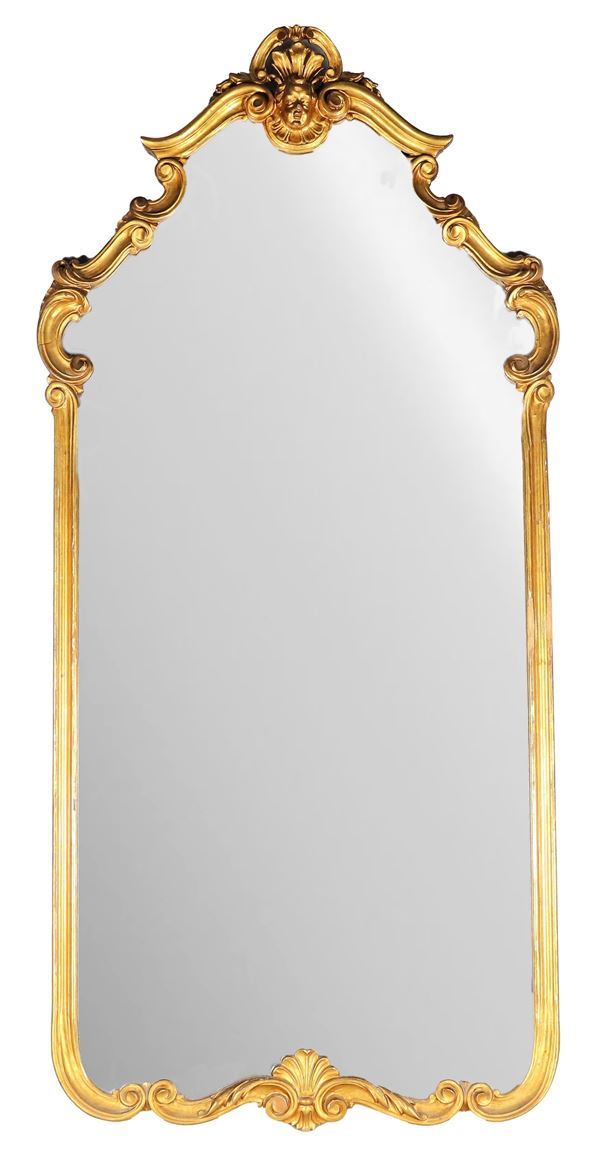 Ancient large mirror in gilded wood and carved with scroll motifs with a sculpture of a cherub's head on the cymatium. Late 19th century