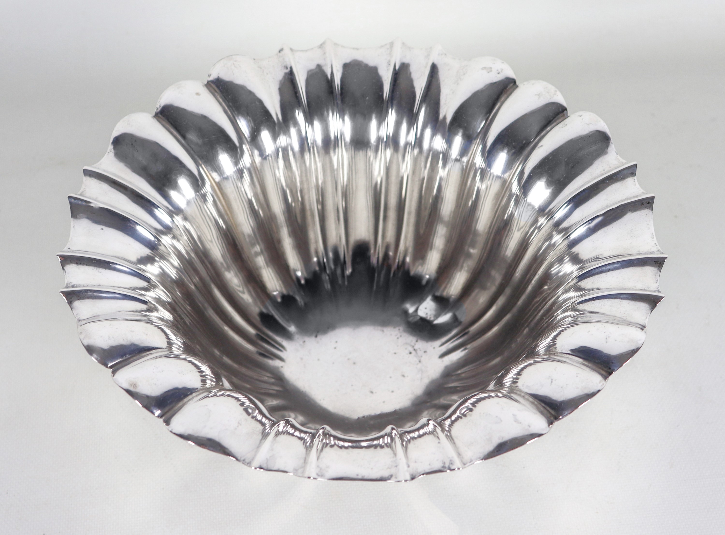 Antico centrotavola tondo in argento con bordo smerlato e baccellato, sorretto da quattro piedini...