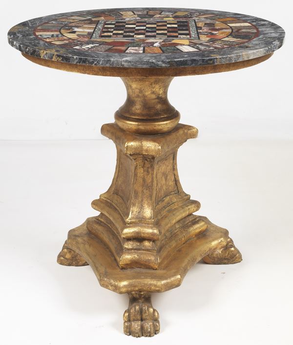 Antico tavolo da centro romano a forma tonda, con piano a tarsie di marmi pregiati con scacchiera al centro, base triangolare in legno dorato e intagliato, sorretta da tre gambe con piedi leonini