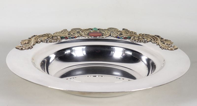 Grande centrotavola in argento, con applicazioni sul bordo di volute dorate e pietre dure. Marcat...