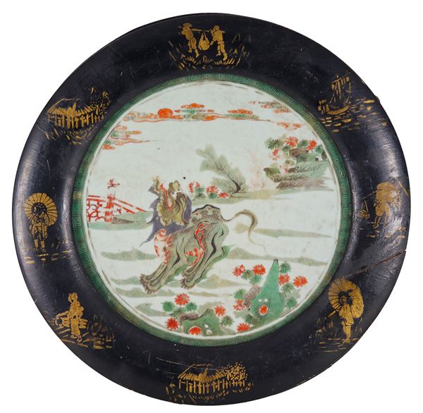 Ancient Chinese round-shaped plaque, in porcelain decorated and colorful with oriental motifs, black lacquered wooden frame with decorations of oriental life scenes in pure gold, slight defect