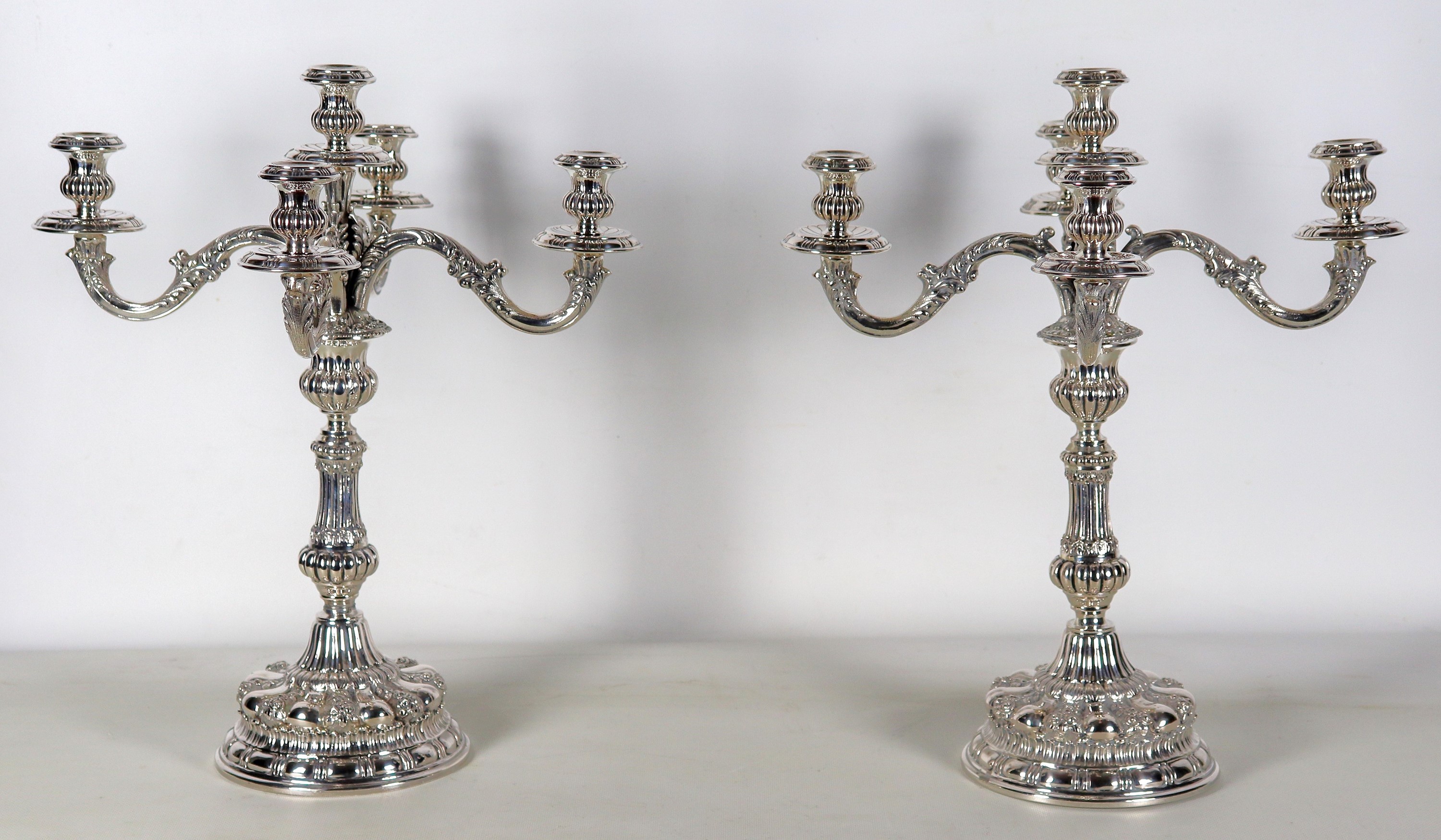 Coppia di candelabri in argento, interamente cesellati e sbalzati a motivi floreali, volute e bac...