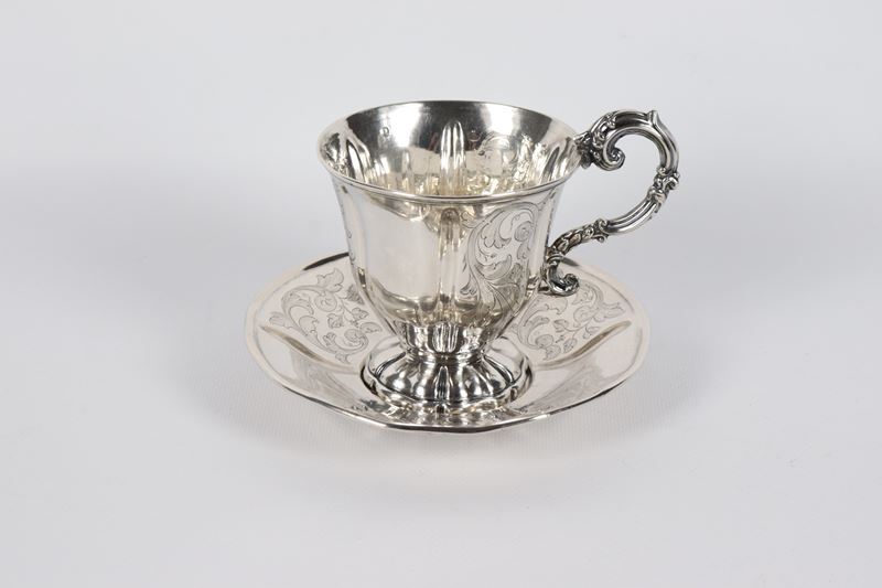 Antica tazza romana in argento con piattino, cesellata e sbalzata a volute floreali con manico ri...