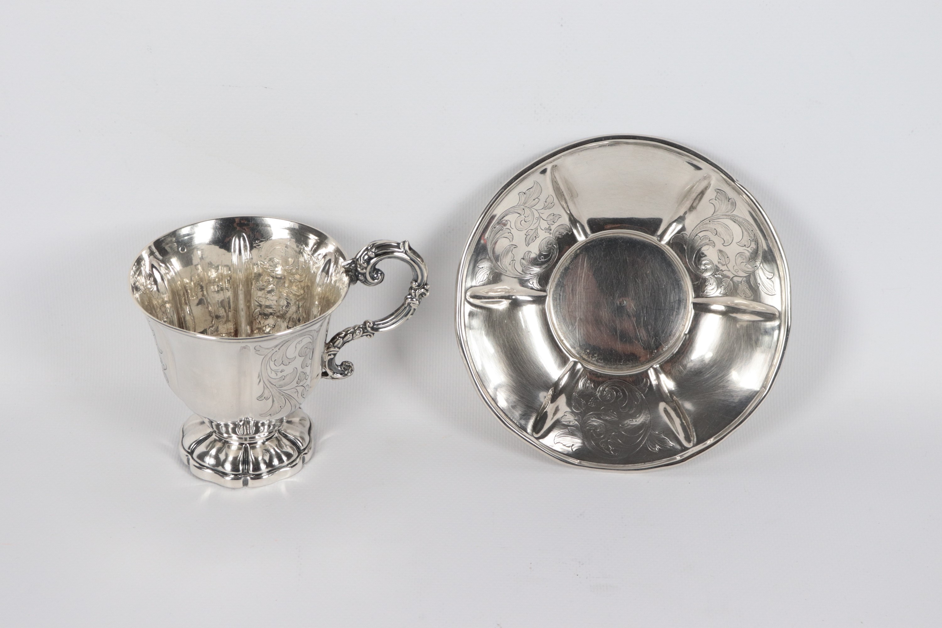 Antica tazza romana in argento con piattino, cesellata e sbalzata a volute floreali con manico ri...
