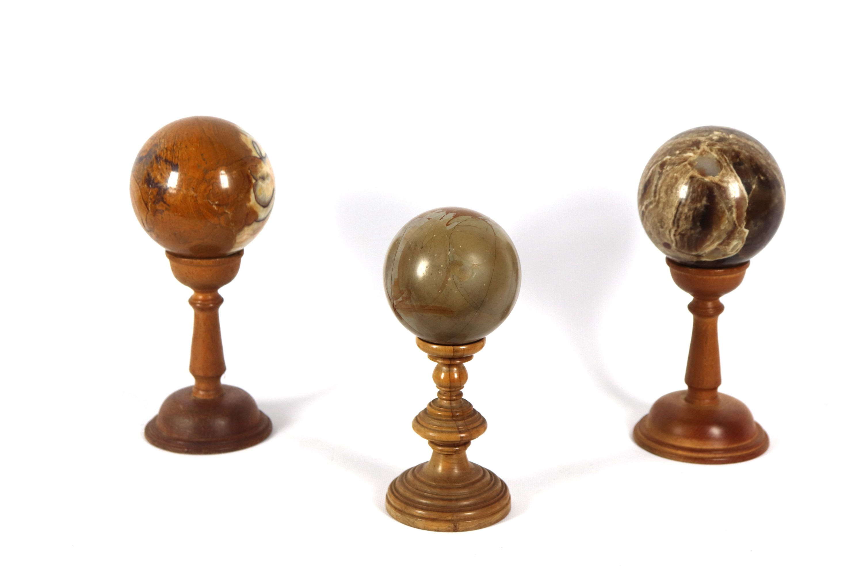 Lotto di tre sfere in vari marmi pregiati, sorrette da basette a colonne tornite in legno di noce