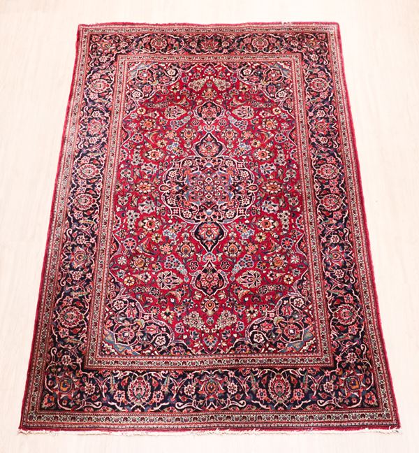 Persian Kashan rug with geometric floral design on red background and blue border. Slight missing parts on the edges of the fringes