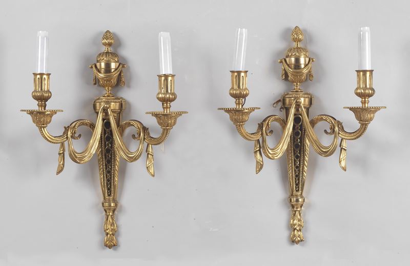 Coppia di appliques francesi in bronzo dorato, sbalzato e cesellato a motivi Luigi XVI di fiocchi...