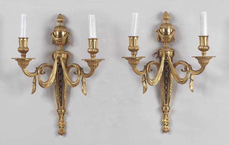 Coppia di appliques francesi in bronzo dorato, sbalzato e cesellato a motivi Luigi XVI di fiocchi...