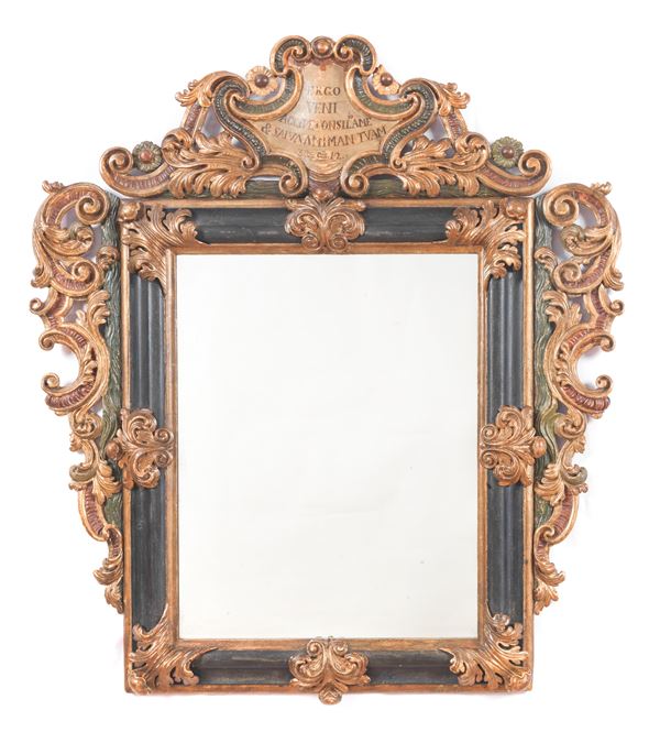 Tuscan mirror in Louis XIV style in lacquered and gilded wood, richly carved with scrolls, acanthus leaves and curls, with an inscription on the top