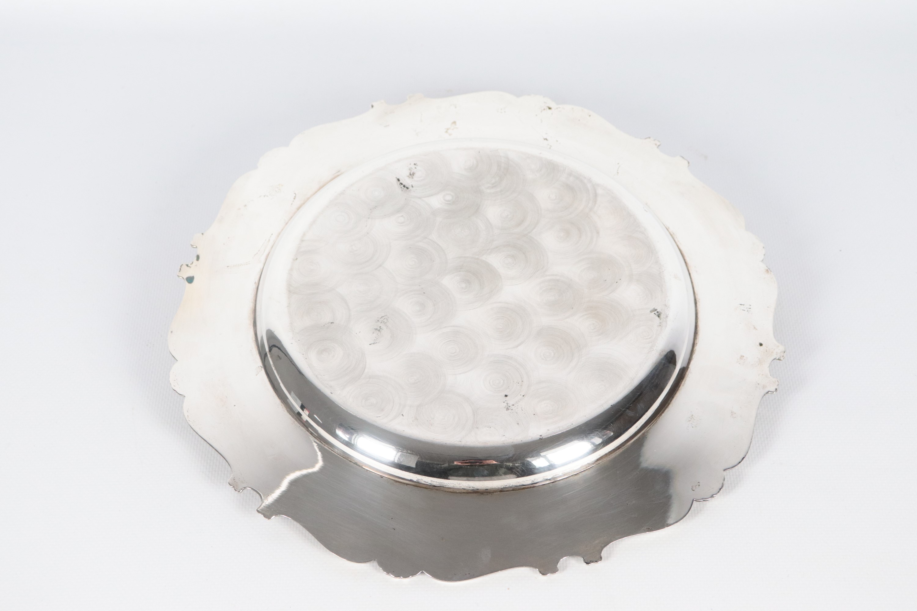 Centrotavola tondo in argento con bordo centinato, cesellato e sbalzato a motivi di volute e conc...