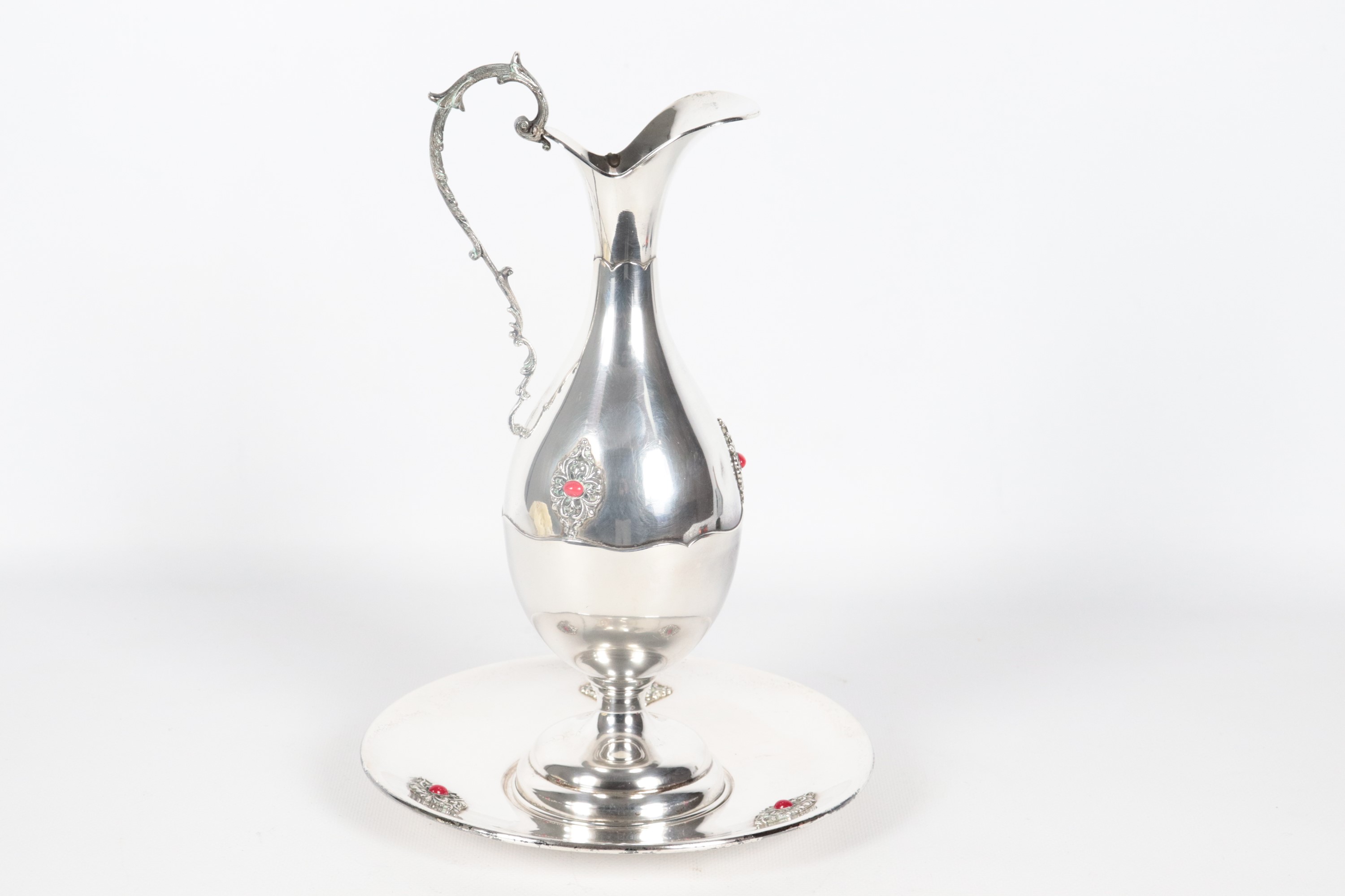 Brocca in argento con sottopiatto, cesellata e sbalzata con applicazioni di pietre rosse, gr. 540