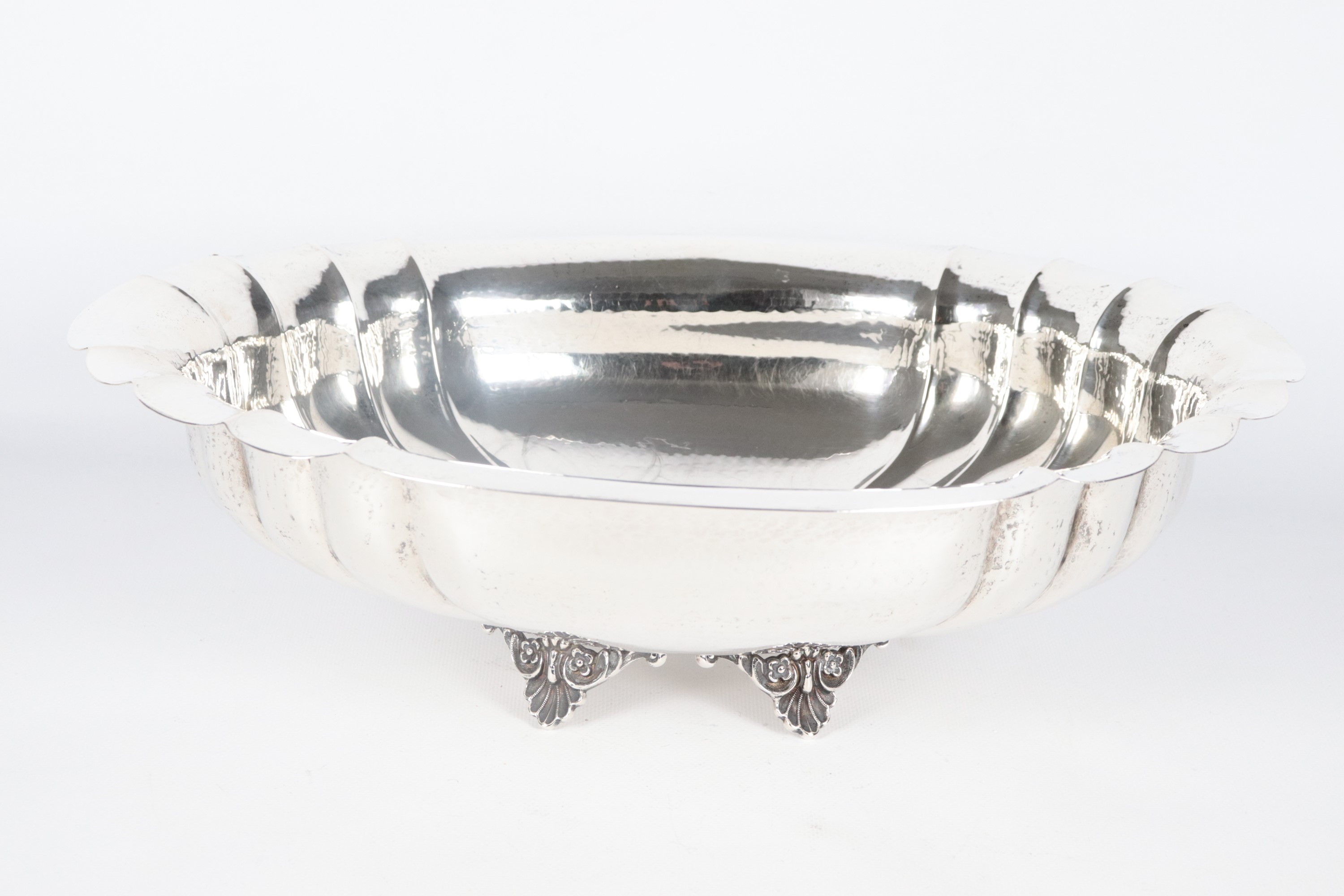 Centrotavola ovale in argento cesellato e sbalzato, con bordo centinato e sorretto da quattro pie...