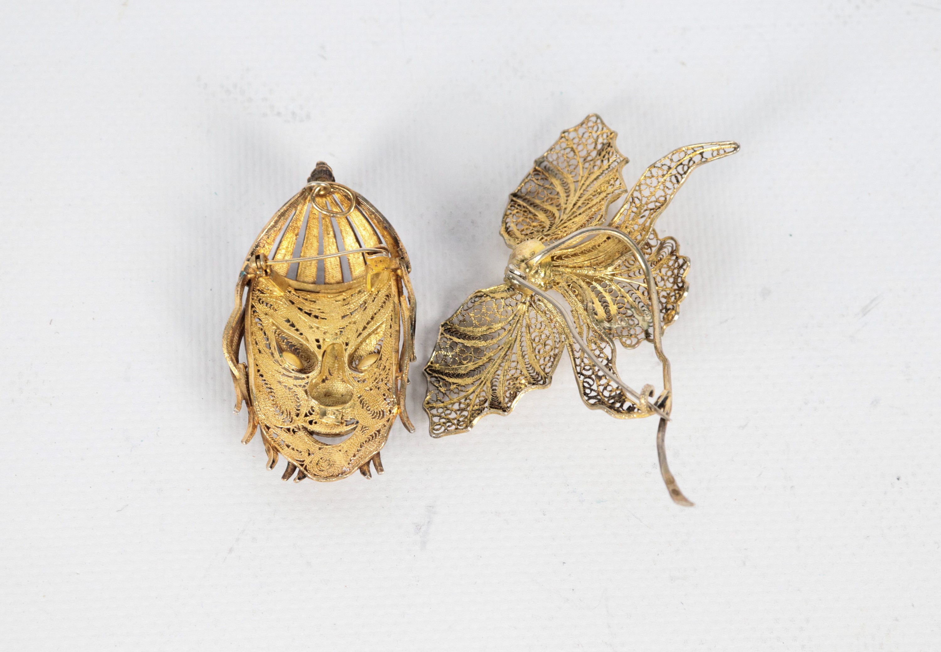 Lotto di due spille in argento filigranato e smalti, una a motivo di foglie e fiore una con volto...