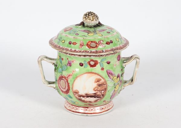 Tazza cinese in porcellana verde con coperchio e due manici, con decorazioni in smalti policromi a rilevo a motivi di farfalle, fiori e medaglioni con paesaggi, lieve difetto al bordo superiore della tazza