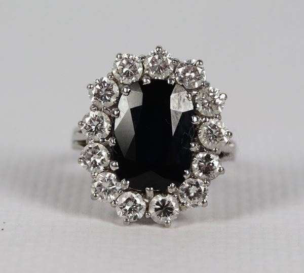 Anello in oro bianco 18kt con zaffiro ovale contornato da tredici diamanti taglio brillante ct 1,30 circa, gr. 8,9