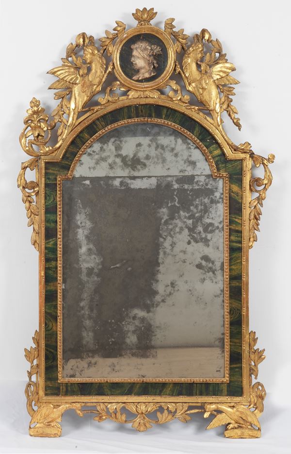 Antica grande specchiera in legno dorato e laccato a finto marmo, riccamente intagliata con volute vegetali, sculture di arpie e medaglione al centro della cimasa, specchio al mercurio. Qualche mancanza