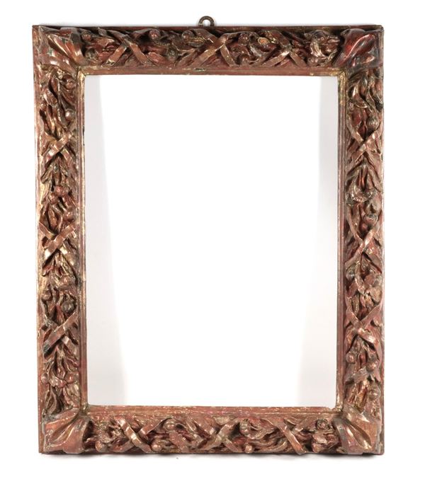 Antica cornice in legno decorato e patinato, interamente intagliata a rilievo a motivi di cordoni intrecciati e frutta